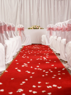 Red carpet with chairs arranged either side dressed with red ribbons, with flower petals scattered over leading to an altar for a civil wedding ceremony at mercure hotels