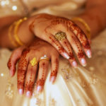 An Indian bride displays the henna artwork on her hands, wearing an ivory coloured dress