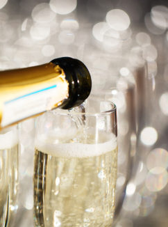 close up of a bottle pouring champagne into glasses with blurred background