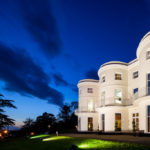 An angled view of the lawn and frontage of the mercure gloucester bowden hall hotel in floodlights at night